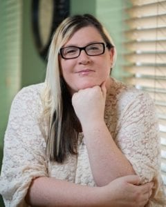 A woman with glasses sitting in front of a window.