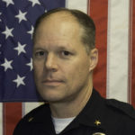 A man in police uniform with an american flag behind him.