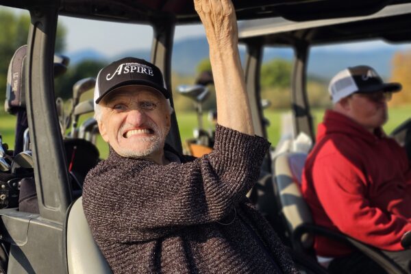 A man sitting in a golf cart waving to the camera.