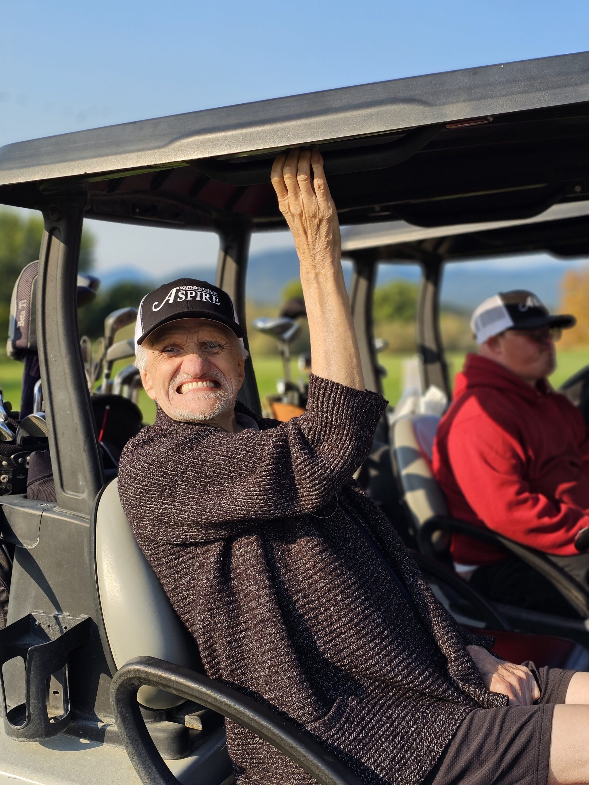 A man sitting in a golf cart waving to the camera.