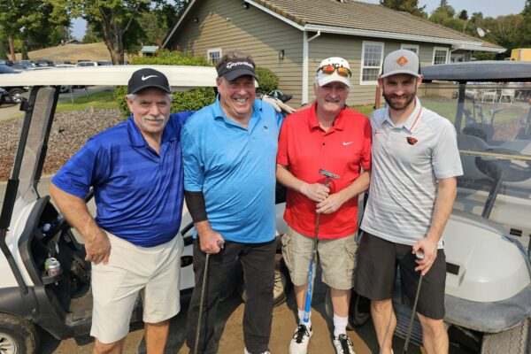 Four men standing next to each other holding golf clubs.