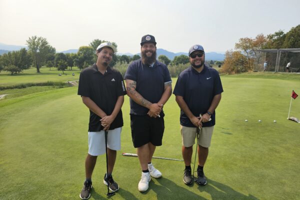 Three men standing on a golf course holding their clubs.