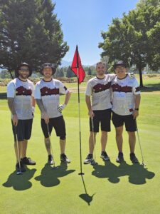 4 Men in matching sports team shirts on golf course next to red flag